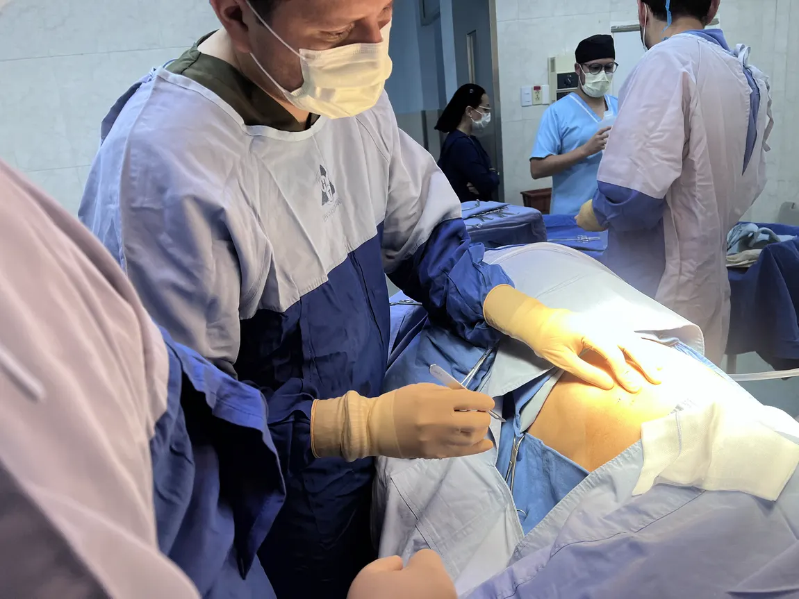Médico haciendo con bisturí la pequeña incisión de entrada en la pared lateral del tórax, con el paciente de lado y cubierto con campos estériles